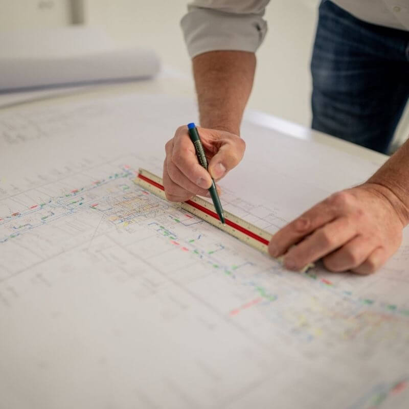 SSN Gebäudetechnik Mitarbeiter zeichnet mit Bleistift und Lineal auf einen Plan, der auf dem Tisch liegt